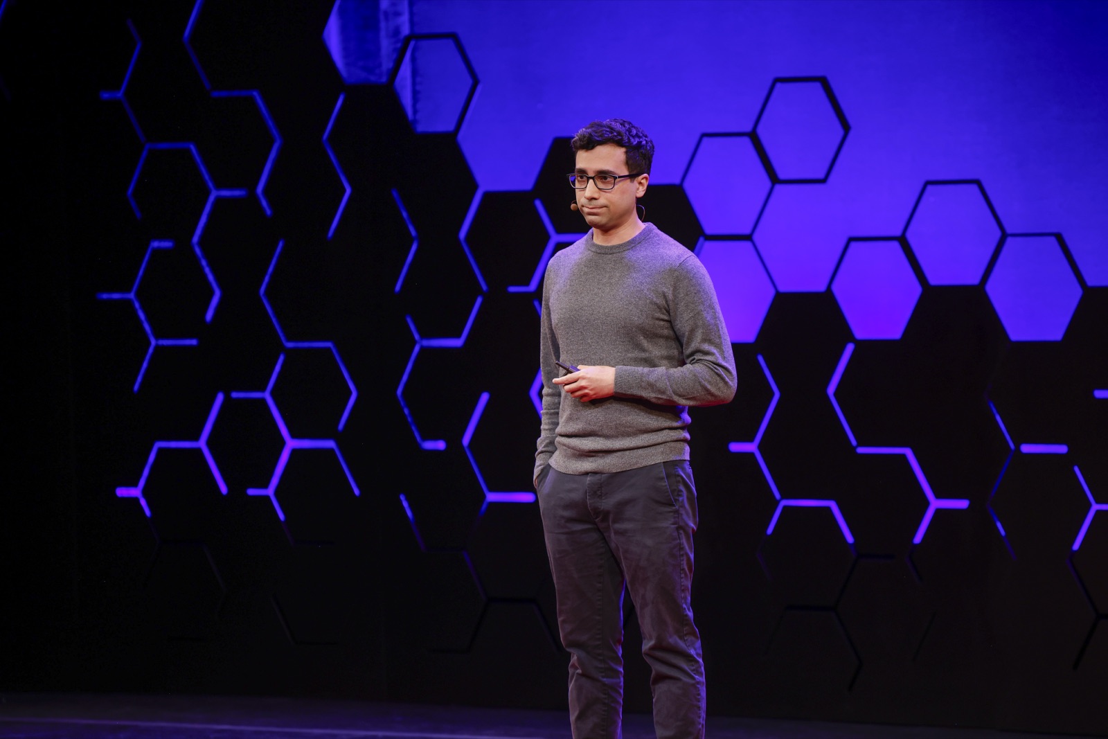 Speaker on the TED AI stage against a violet hexagon backdrop